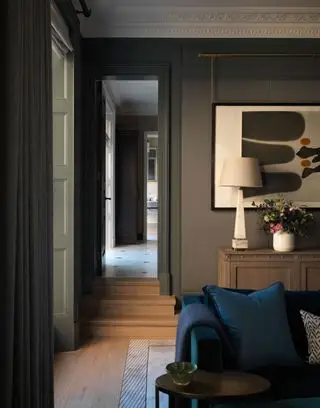 밝은 색상의 현대적인 그림, 램프 및 꽃병, 파란색 소파 및 쿠션, 나무 바닥을 갖춘 어두운 페인트 거실