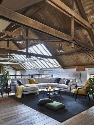 アーチ型天井のロフト リビング ルーム、青い敷物の上に灰色のセクション、肘掛け椅子、ペンダント ライト