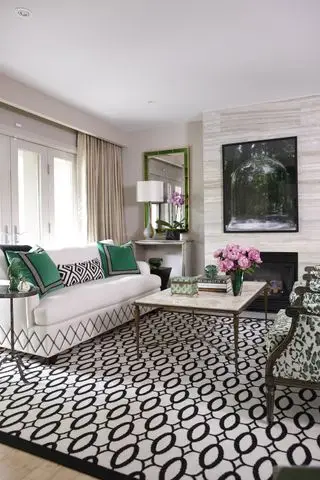 Salón blanco con sofá blanco, cojines verdes y alfombra geométrica en blanco y negro