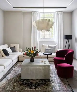 Un salon minimaliste avec des murs blancs, une suspension blanche et un fauteuil en velours rouge