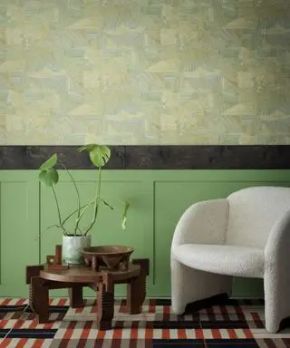 Sala de estar con papel tapiz de dado atelier en papel tapiz sterno de matthew burrows, paneles pintados de verde, sillón boucle, mesa de centro de madera oscura, alfombra a rayas rojas, crema y negras