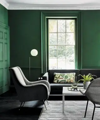 Salón verde con sofá gris, sillón y alfombra, mesa de centro blanca, cojín estampado, suelo negro, lámpara de pie, los colores de pintura verde favoritos de los diseñadores, comedor verde oscuro con pintura Little Greene
