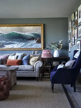 Salón con paredes de color gris azulado, una silla de terciopelo azul oscuro y un gran cuadro de paisaje marino.