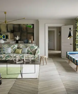 Un sofá con estampado verde en una larga sala de estar con suelo de madera en forma de espiga.