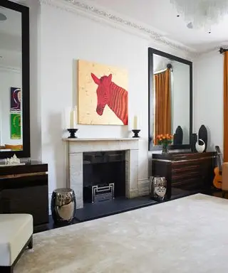 Dos espejos a cada lado de una chimenea con coloridas obras de arte y una alfombra color crema.