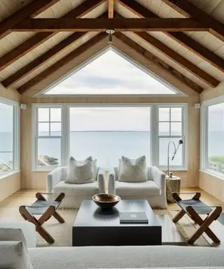 Una sala de estar con techos abovedados y grandes ventanales triangulares, sillones blancos y taburetes de cuero negro.