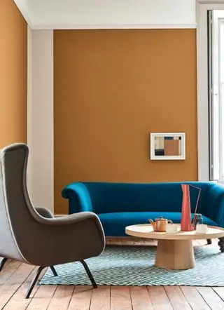 Ideen für Wohnzimmerfarben mit orangefarbenen Wänden, einem blauen Sofa und einem gemusterten Teppich.