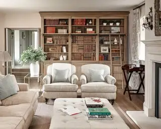 Pomysły na formalny salon z tradycyjnymi kremowymi fotelami i drewnianymi półkami na książki