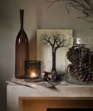 Efterårsmantelideer med brun glasflaske og lysestage, fyrrekogler i en orkanvase og træmaleri