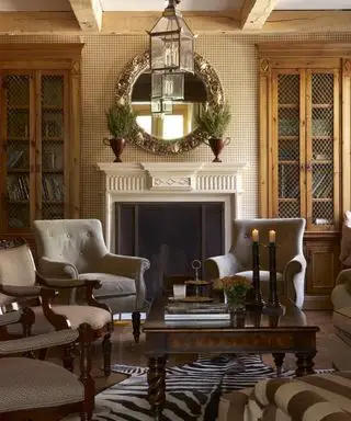 Efterårs kaminidéer med et brunt traditionelt skema, creme kaminhylde med løvfyldte træurner og cirkulært spejl