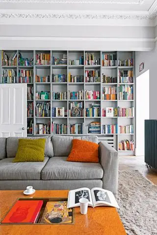 Weißes Wohnzimmer mit grauen eingebauten Bücherregalen und grauem Sofa mit Couchtisch aus Holz