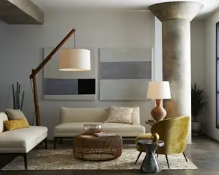 Grandes luminárias de piso e mesa de madeira ilustram como planejar a iluminação da sala em um esquema de cores neutras com grandes pilares de concreto.