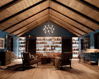 Kichler Lighting mostra como planejar a iluminação da sala de estar com teto e parede em uma grande sala azul escura com estantes embutidas e cadeiras de couro.