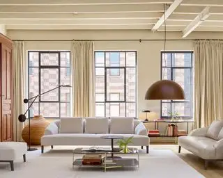 Um exemplo de como planejar a iluminação da sala, com sofás brancos, luminárias de chão pretas e uma grande luminária pendente em frente a três grandes janelas.