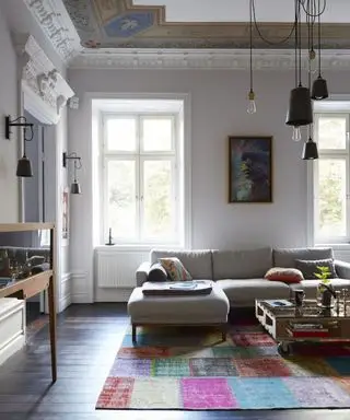 Uma sala branca, tapete multicolorido e sofá bege com iluminação variada.