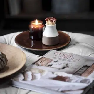 Kerze auf einem Teller und Streichholzglas auf einem Fußhocker mit Buch