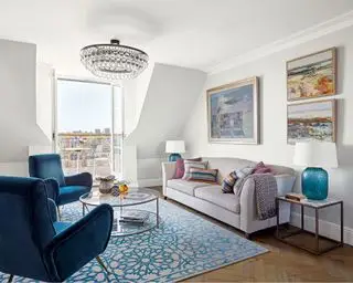 Lille stuebelysningsideer i en hvid hems stue med blå lænestole, neutrale sofaer og tagudsigt.