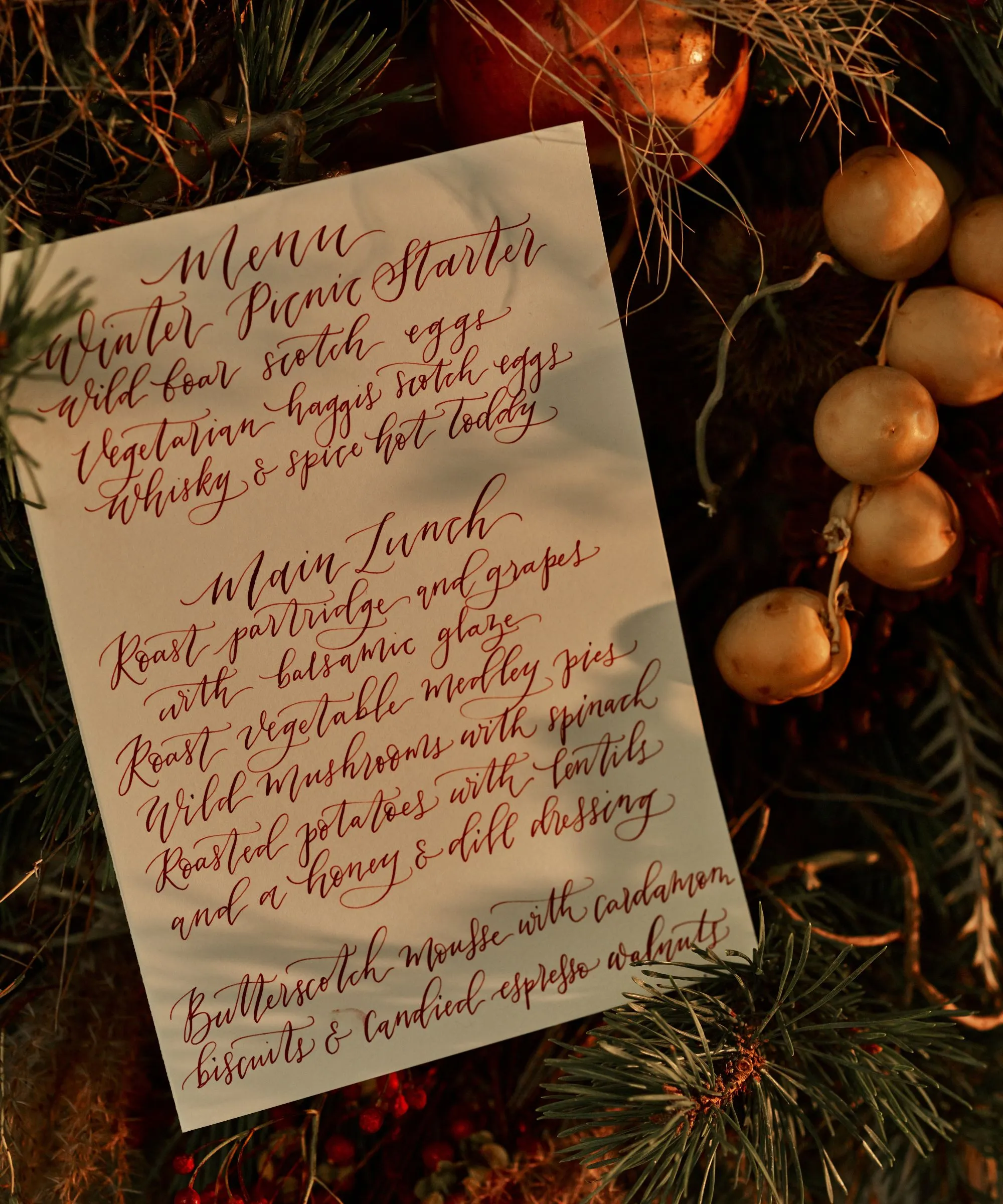 תפריט ארוחת ערב בכתב יד לצד זר אורן ופירות יער' loading='lazy' title=