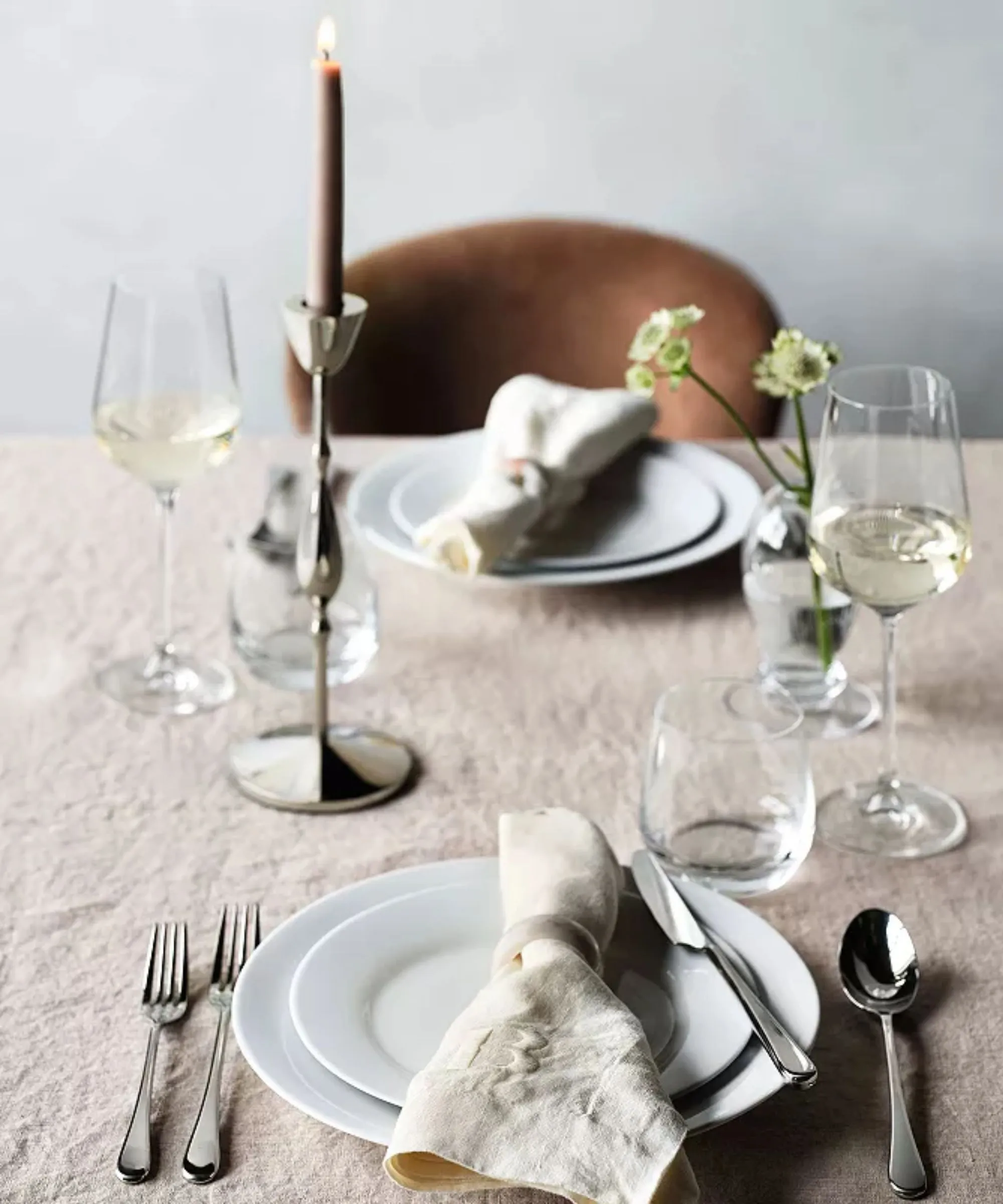 Toalha de mesa de linho natural com guardanapos combinando, pratos brancos, talheres de prata e castiçais cônicos de prata' loading='lazy' title=