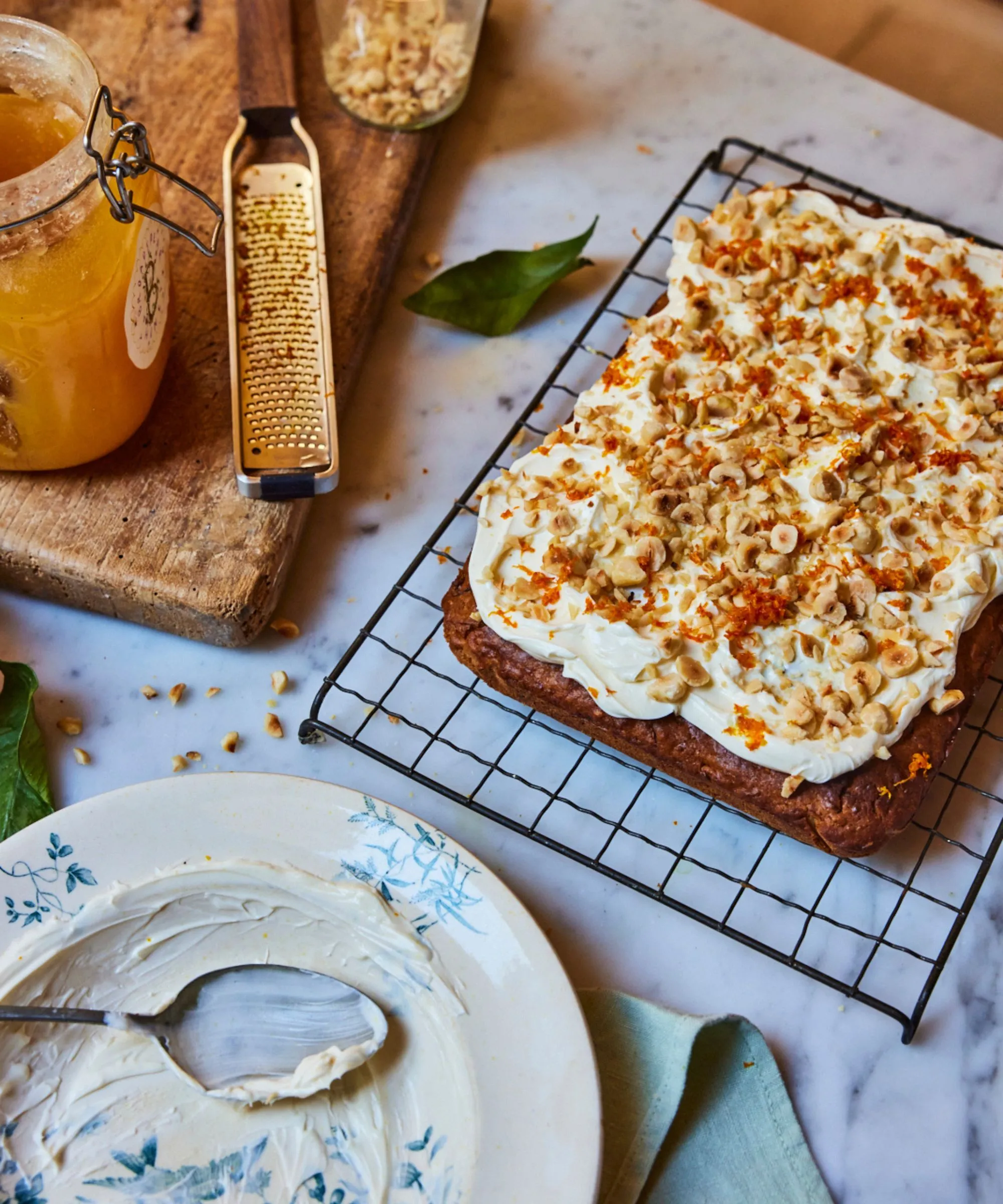 皿とスプーンの木の板の横にあるワイヤーラックに白いフロスティングとナッツのようなトッピングをしたパースニップケーキとゼスターと蜂蜜のポット' loading='lazy' title=