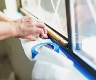 Quelqu'un applique du ruban adhésif pour peintres sur une fenêtre