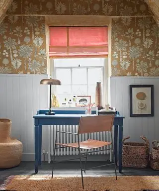 Blåt skrivebord med læder- og metalstol, vindue med rød persienn, okkerblomstret tapet, lyseblå malet panel, metallisk bordlampe, tekstureret tæppe og vævede kurve