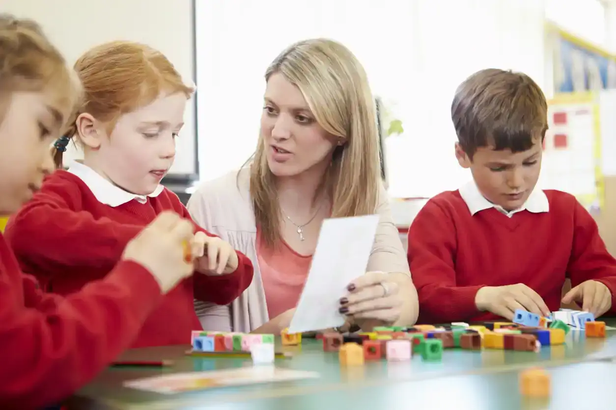 Primary School Pupils And Teacher Working With Coloured Blocks
