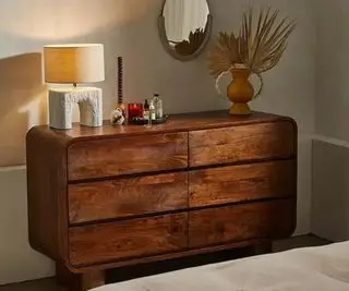 회색 침실 벽 위에 장신구를 얹은 Urban Outfitters 원목 서랍장.