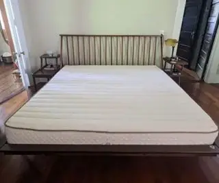 Matelas en latex biologique PlushBeds Botanical Bliss sur un lit contre un mur blanc.