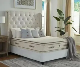 Matelas en latex biologique PlushBeds Botanical Bliss sur un lit contre un mur blanc.