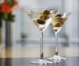 Un verre à martini avec des olives et quelques fleurs en arrière-plan