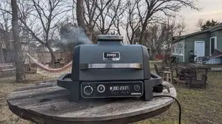 La camera di fumo del barbecue da esterno Ninja Woodfire, piena di pellet, era posizionata su un tavolo da giardino in legno