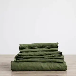Ensemble de draps en lin vert forêt contre le mur d'une chambre.