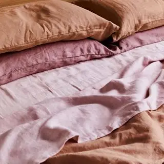 Pacchetto di biancheria da letto in terracotta, acqua di rose e lavanda su un letto.