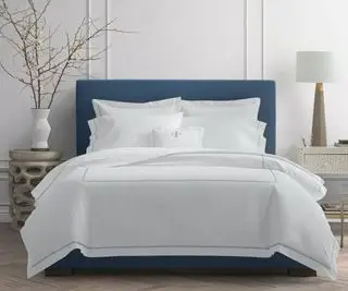 Biancheria da letto tratteggiata su un letto contro un muro bianco.