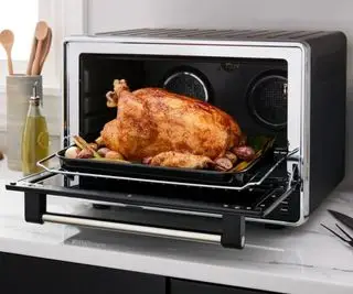 Un poulet rôti dans un four à convection de comptoir KitchenAid avec friteuse à air sur un comptoir de cuisine.