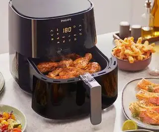 Friteuse à air Philips Essentials XL sur un comptoir de cuisine, remplie d'aliments frits à l'air.