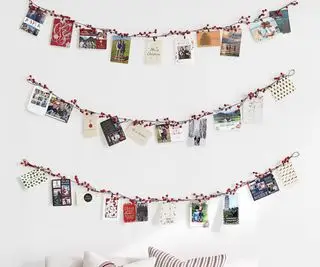 Uchwyt na kartki świąteczne w kształcie jagodowej girlandy na białej ścianie.