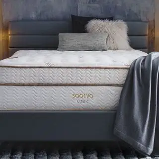 Matelas Saatva Classic avec un jeté gris contre un mur gris.