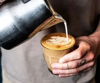 Milchschaum wird in eine Kaffeetasse gegossen
