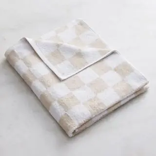 Toalla de baño de rizo blanca y avena contra una pared blanca.