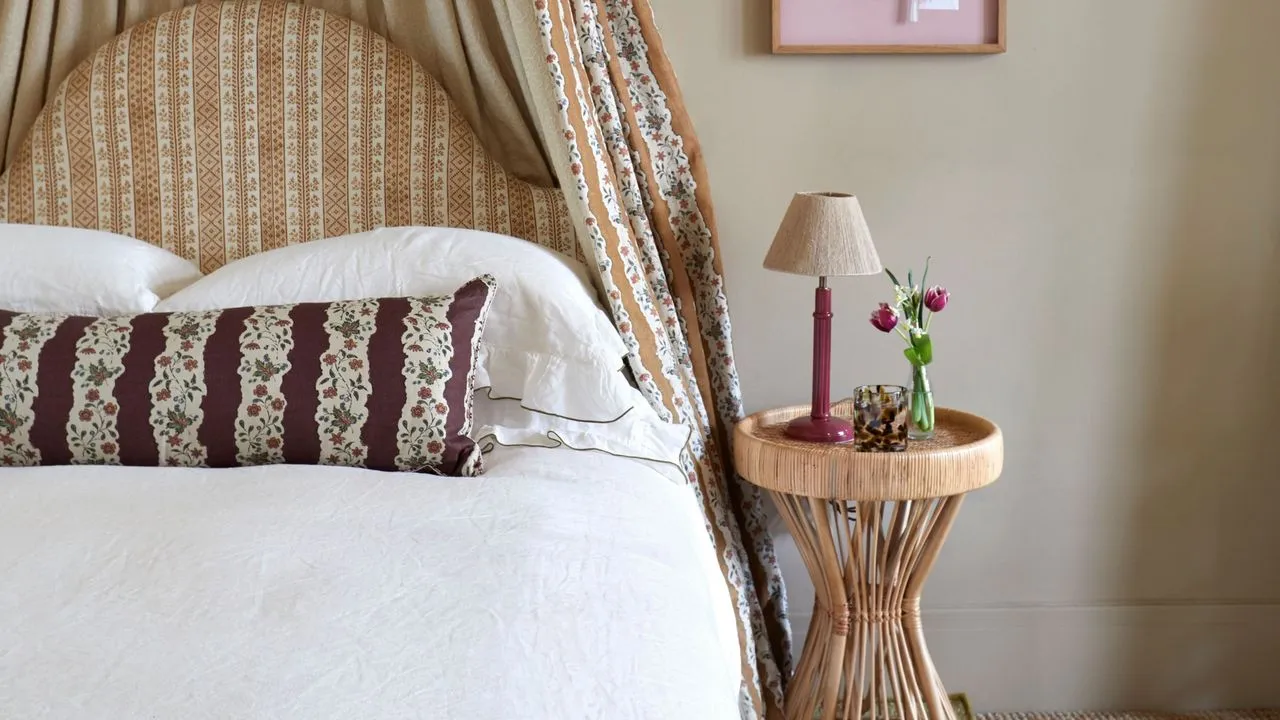 Texturované stínidlo na lakovaném podstavci z oxblood posazené na sochařském odkládacím stolku z přírodních vláken uvnitř ložnice s neutrálním vzorem' loading='lazy' title=