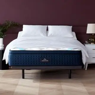 Colchão DreamCloud numa cama com almofadas encostadas a uma parede escura.