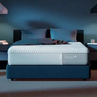 Colchão de neve Casper Wave Hybrid em uma cama com travesseiros contra uma parede azul.