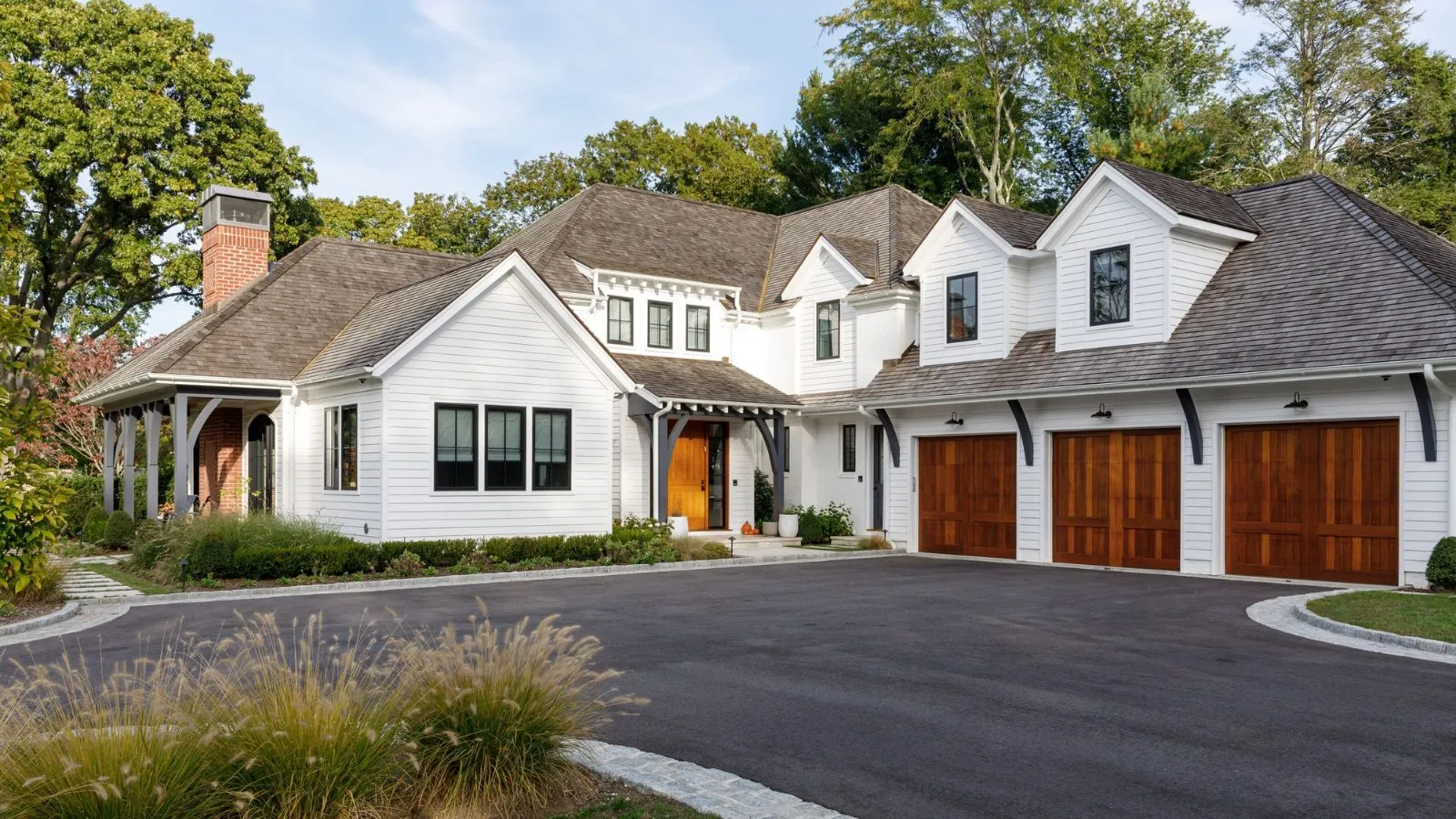 Udvendigt billede af L-formet hjem med tredobbelt garage med spidse tagudhæng og indkørsel' loading='lazy' title=