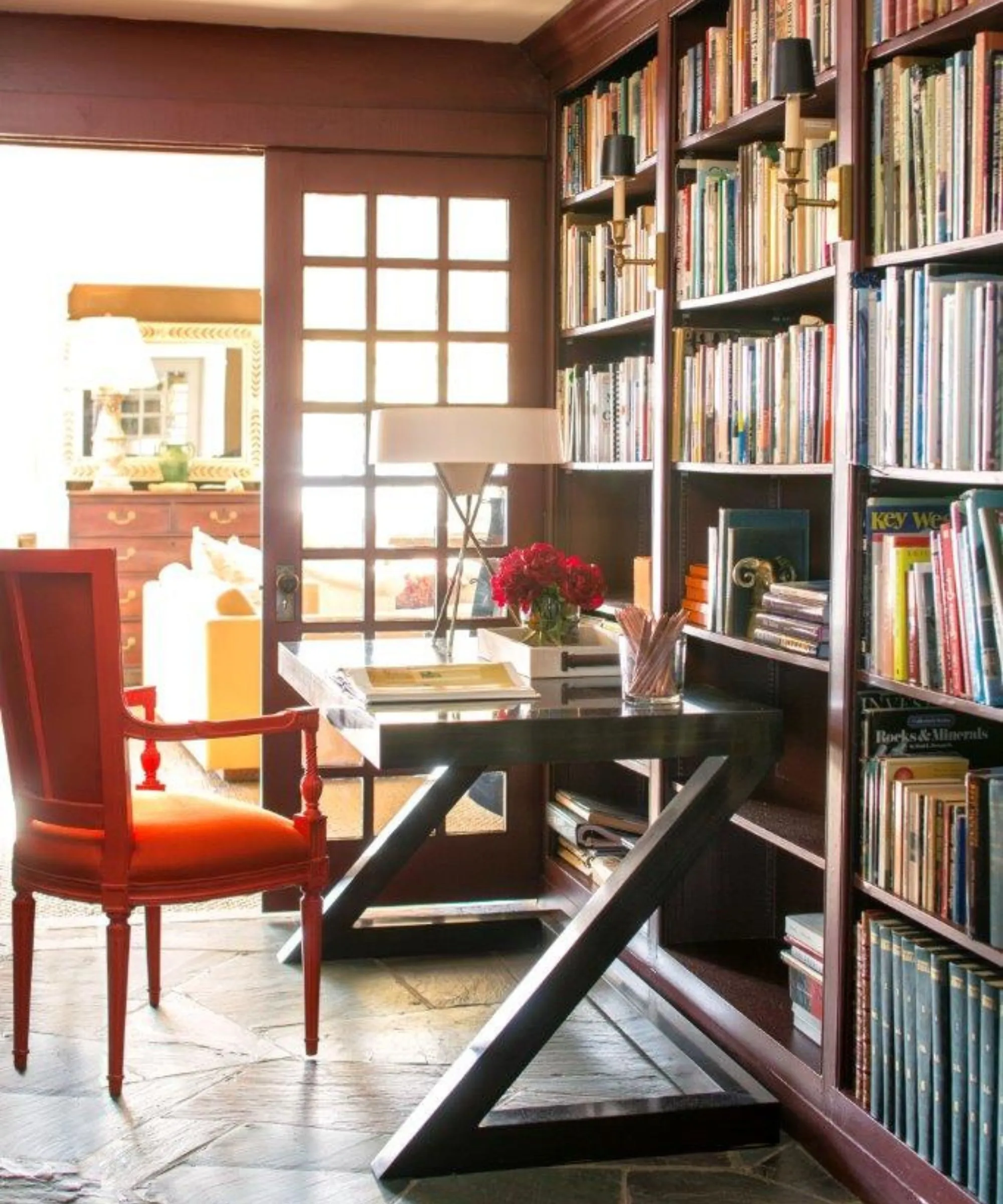 ספרייה ביתית עם קירות בצבע שזיף וארונות מלאים בספרים שולחן כתיבה שחור עם כיסא אדום בוהק' loading='lazy' title=