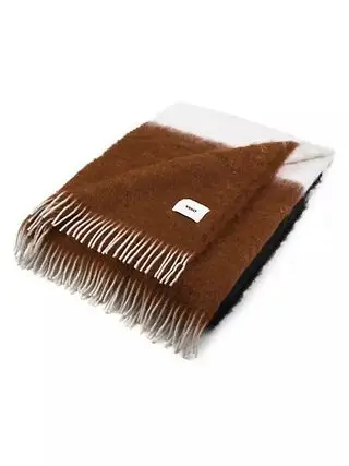 Une couverture en laine marron et crème pliée sur fond blanc