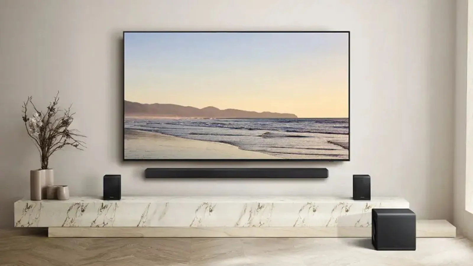 Samsung HW-QS750F Soundbar Woofer og surround højttalere i dæmpet stue omkring tv på marmorstativ ved siden af ​​planter.' loading='lazy' title=