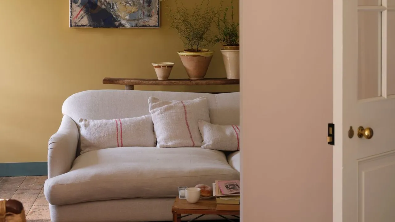 Soggiorno con pareti gialle tenui, divano color crema e pavimenti in legno' loading='lazy' title=