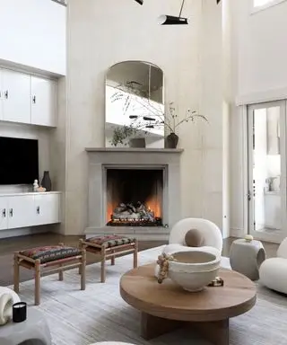 Grand miroir sur cheminée en béton moderne dans le salon avec tapis gris, table basse ronde en bois et tabourets décoratifs